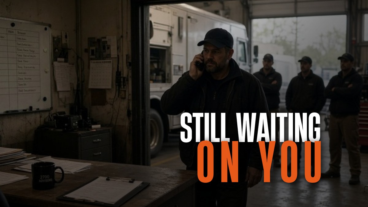 - Service business owner on the phone in his shop office while three crew members wait in the garage bay behind him, overlaid with the words "Still Waiting On You."